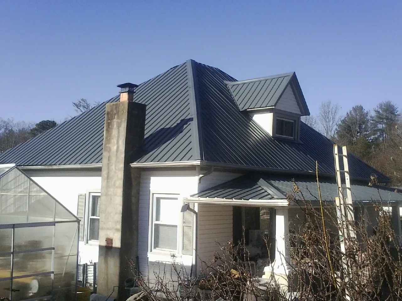 Dark blue standing seam metal roof on a white farmhouse with dormer — Slate & Tile Roof Repair by Roofing Brothers in Primm Springs