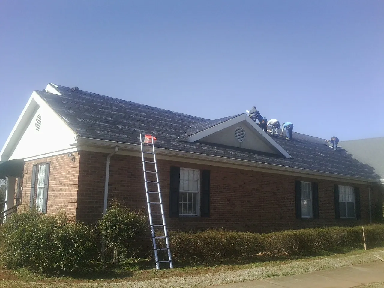 Crew tearing shingles off a brick ranch roof with a ladder set — Emergency Roof Repair work by our crew in Primm Springs