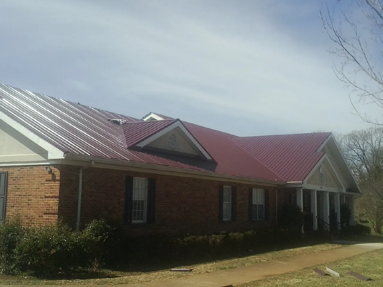 Red metal roof with gabled entries on a long brick building, from a Hail Damage Roof Repair job in Primm Springs