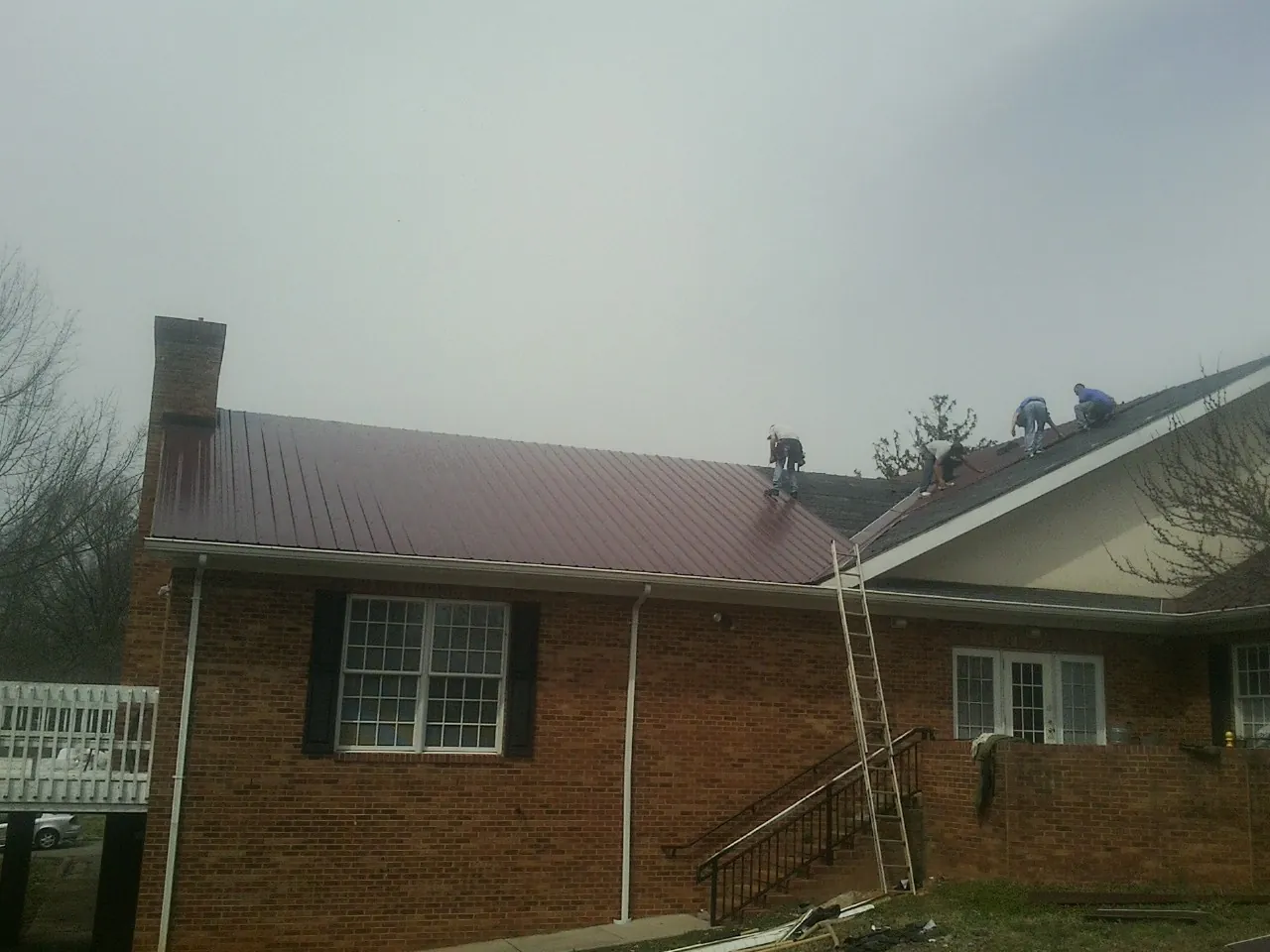 Crew setting red metal roofing panels on a brick home in Primm Springs