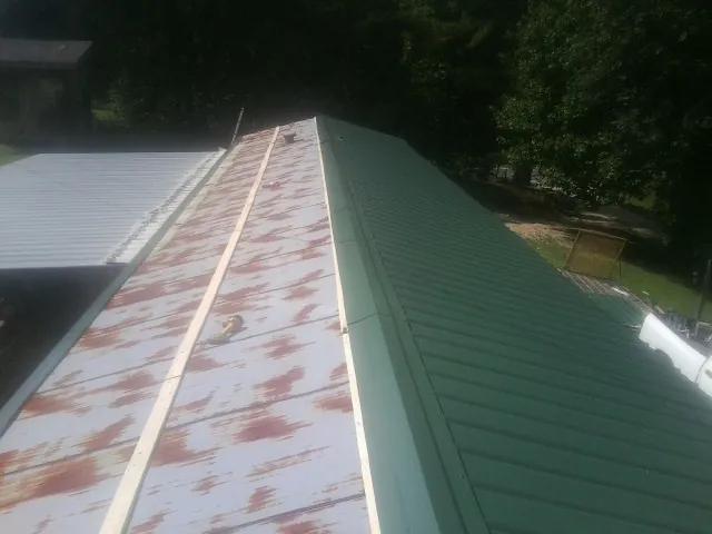Old rusted panels beside newly installed green metal roofing — Wind Damage Roof Repair by Roofing Brothers in Primm Springs