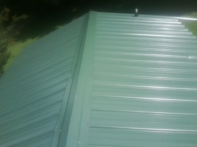 New green metal panels meeting at the ridge of a roof — Flat Roof Repair work by our crew in Primm Springs