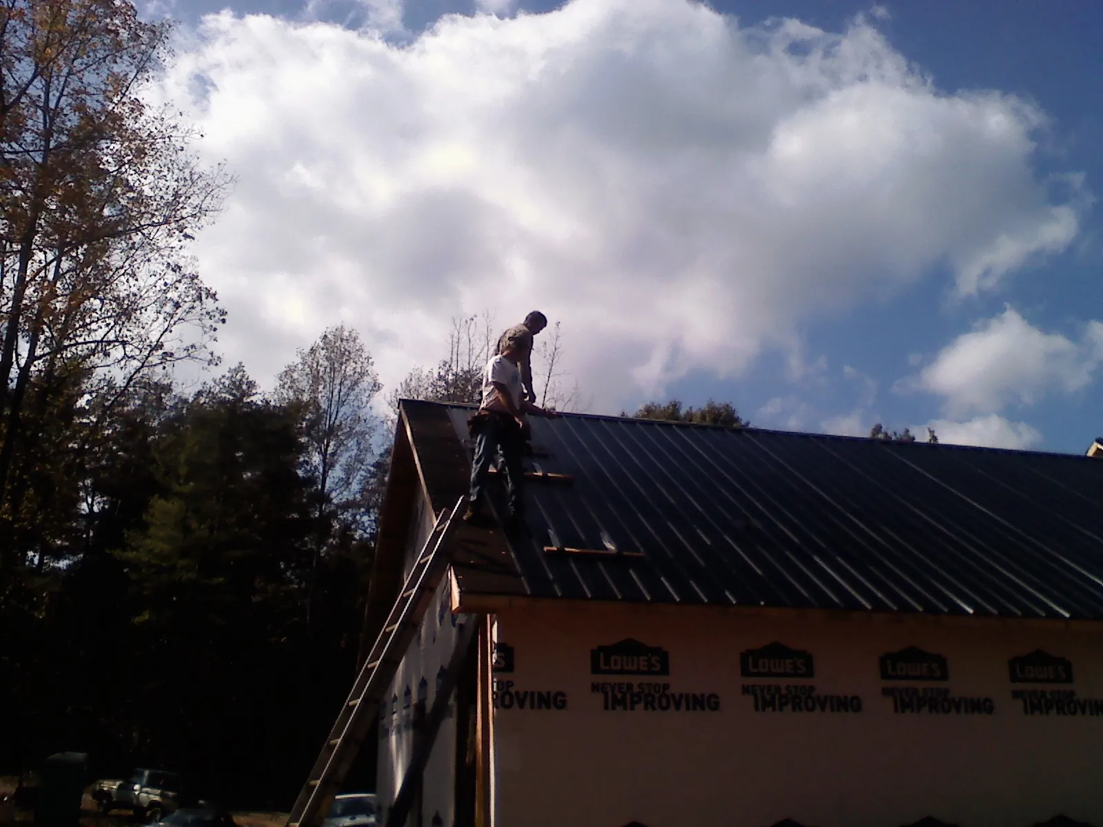 Roofer fastening dark metal panels high against a cloudy sky, from a Roof Inspection job in Primm Springs