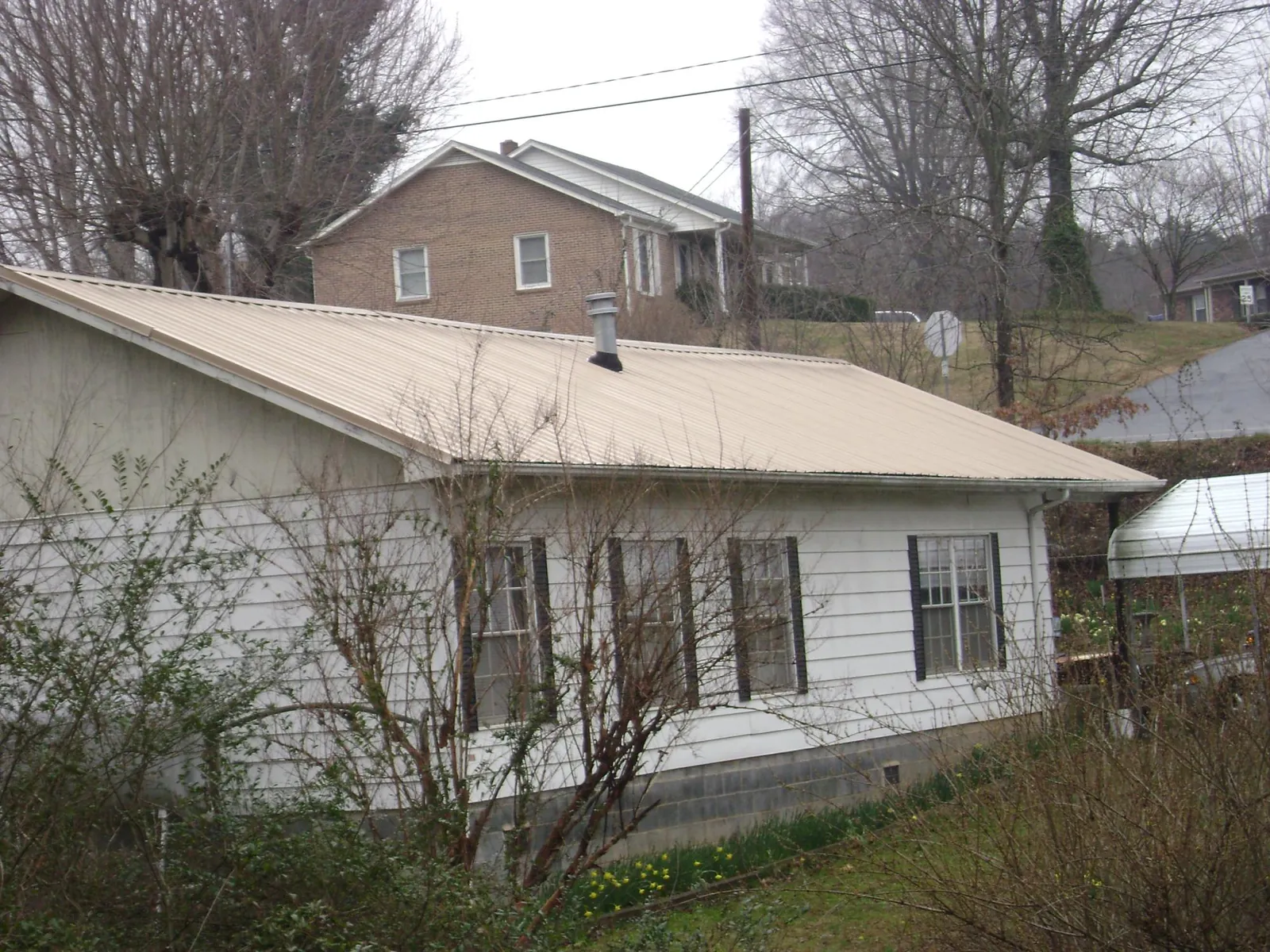 Tan metal roof on a white sided house set into a hillside — Commercial Roofing by Roofing Brothers in Primm Springs